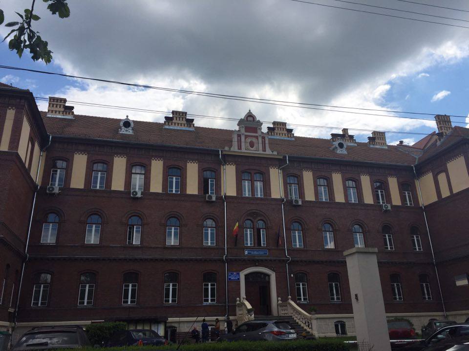 Casa Învăţătorului Cluj, o clădire impozantă din cărămidă roșie cu detalii arhitecturale istorice și ferestre mari.