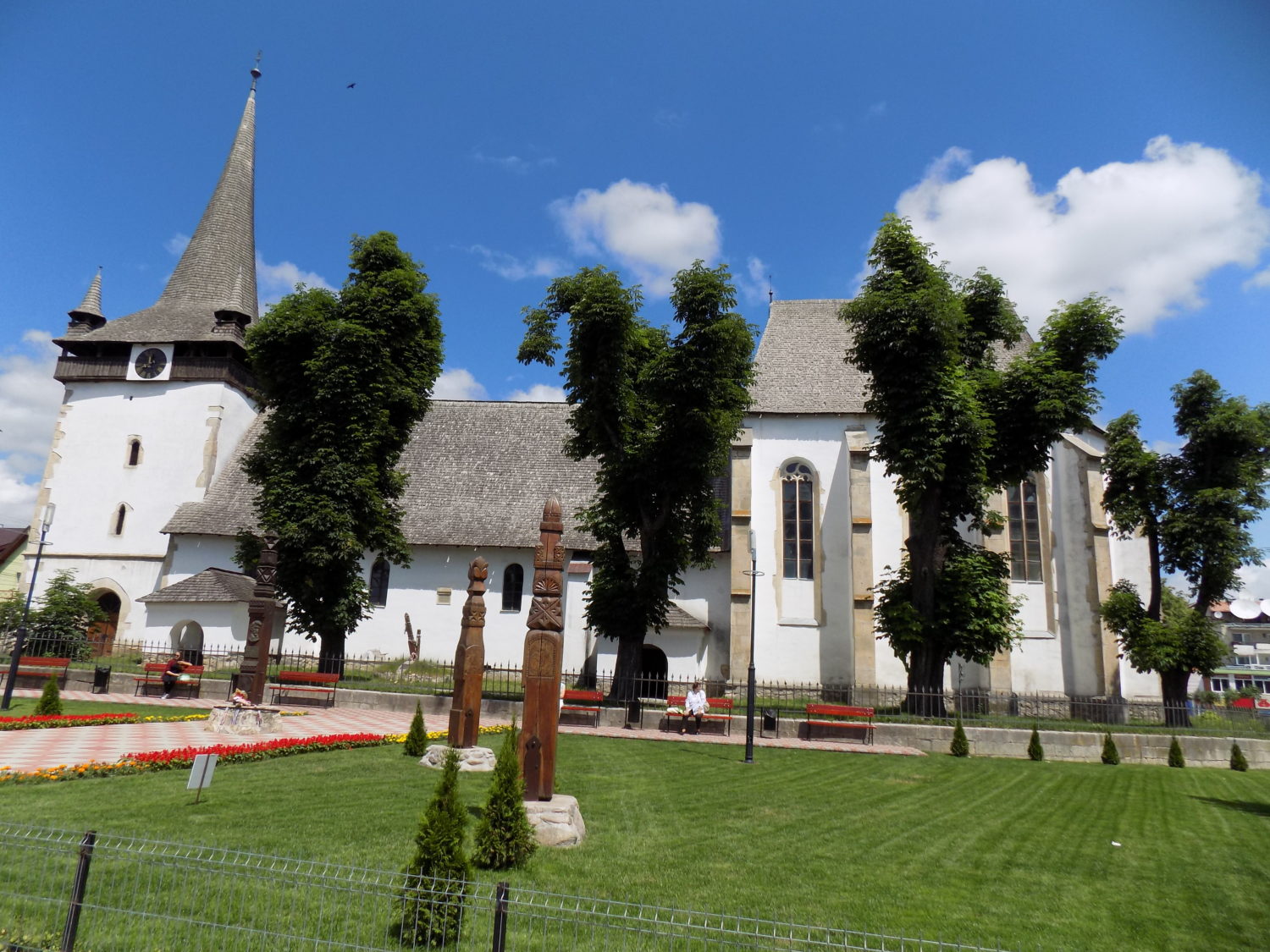 Biserica Reformat-Calvina Huedin, o cladire alba cu turn inalt si acoperis din sindrila, situata intr-un parc amenajat cu monumente