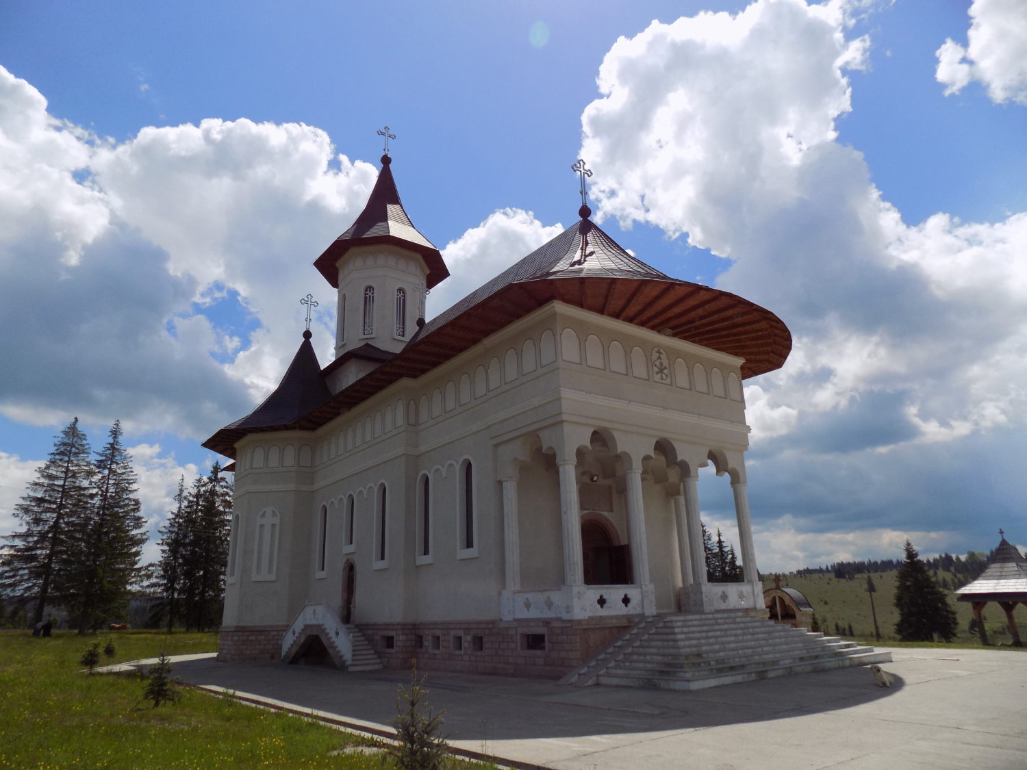 Manastirea Rasca Transilvana, o biserica alba cu acoperis rosu si pridvor sculptat, situata intr-o zona montana deschisa