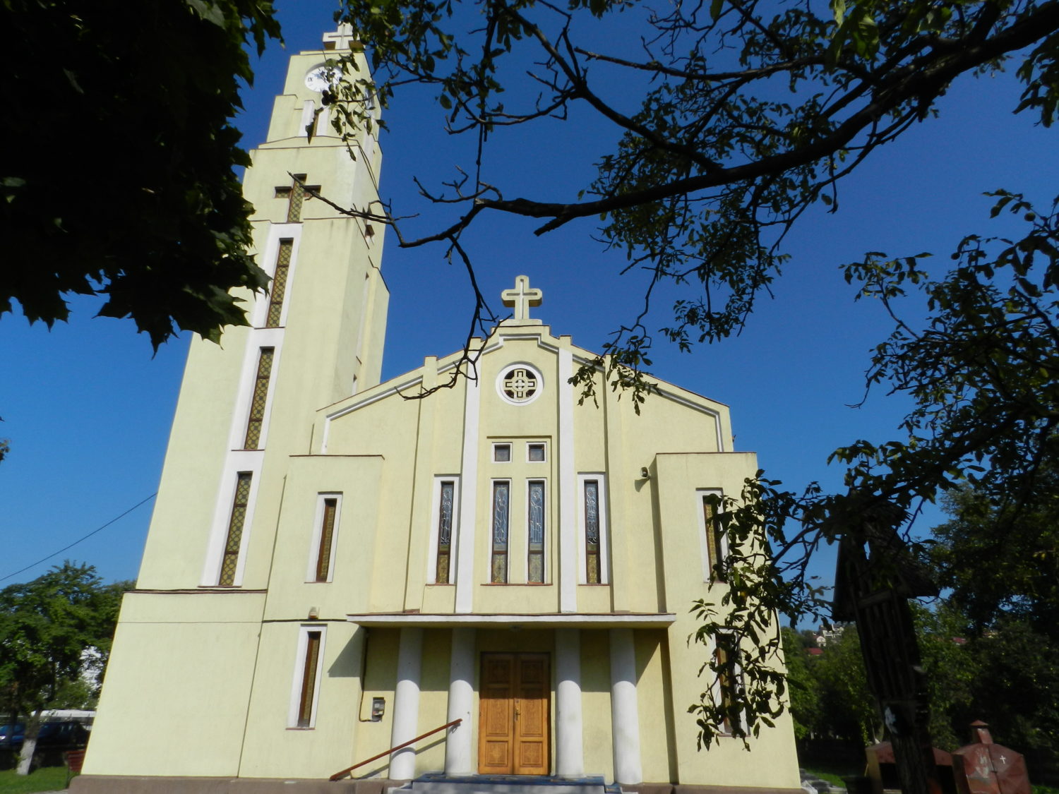 Biserica Ortodoxa Buna Vestire Cluj Napoca, o cladire de culoare deschisa cu un turn inalt si cruci pe fatada, inconjurata de copaci