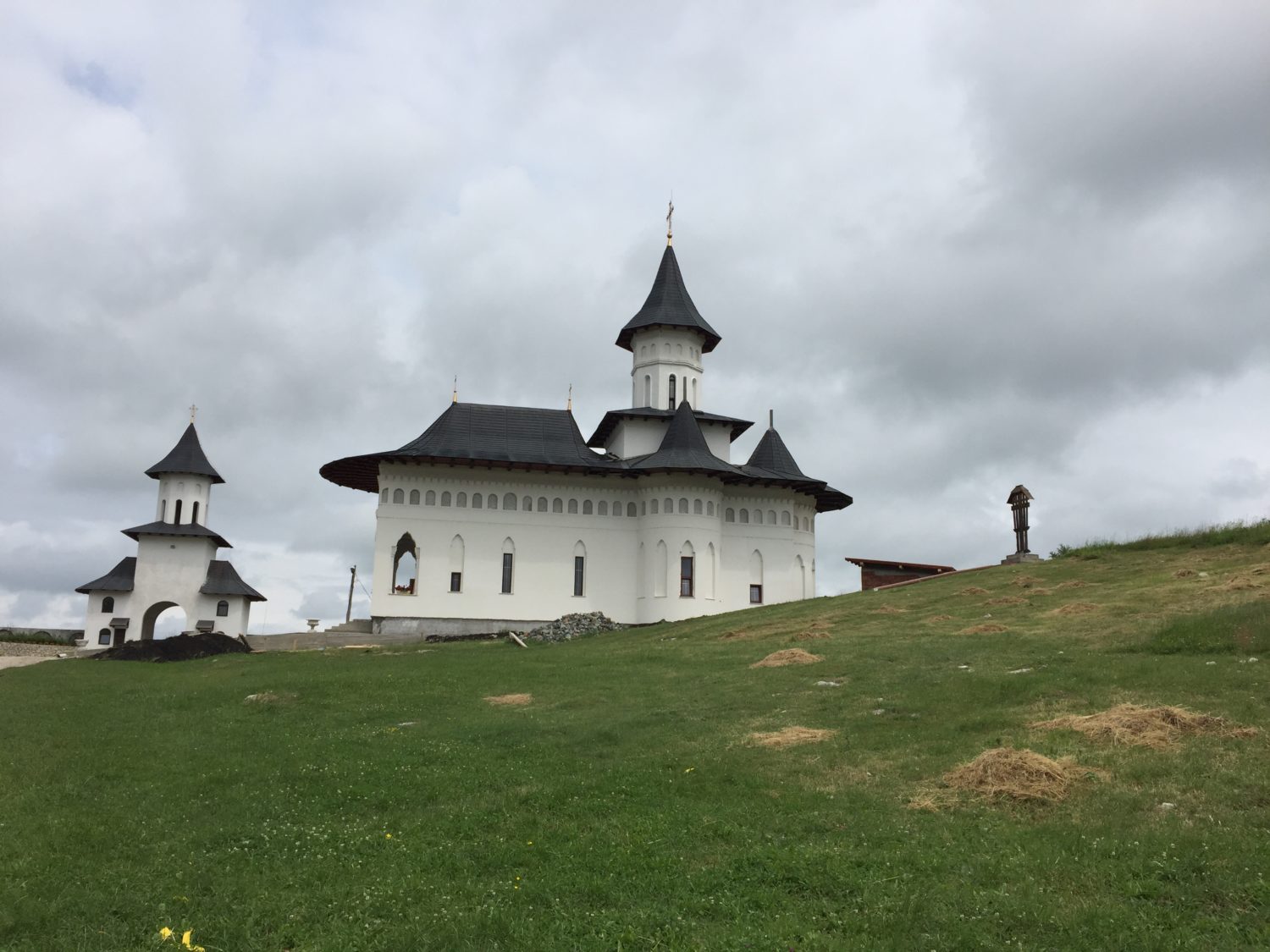 Manastirea Schimbarea la Fata Cheile Turzii, o cladire alba cu acoperisuri negre, situata pe un deal verde, intr-o zona linistita.