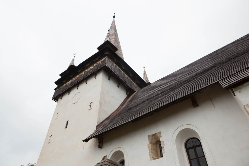 Biserica Reformat-Calvina Valeni, o cladire alba cu acoperis de sindrila si turn inalt din lemn, cu detalii arhitecturale traditionale.