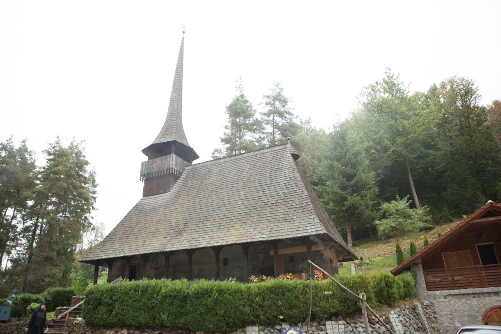 Manastirea Nasterea Maicii Domnului Ciucea, o biserica traditionala din lemn cu turn inalt, amplasata intr-o zona verde si impadurita.