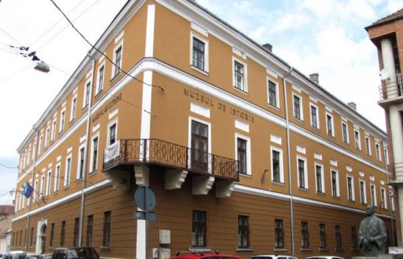 Palatul Muzeului de Istorie Cluj, o clădire istorică maro și albă cu fațadă detaliată și un balcon, situată la colțul unei străzi.