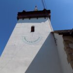 Turnul cu ceas solar al Bisericii Reformat-Calvina Sâncraiu, proeminent pe fundal albastru.